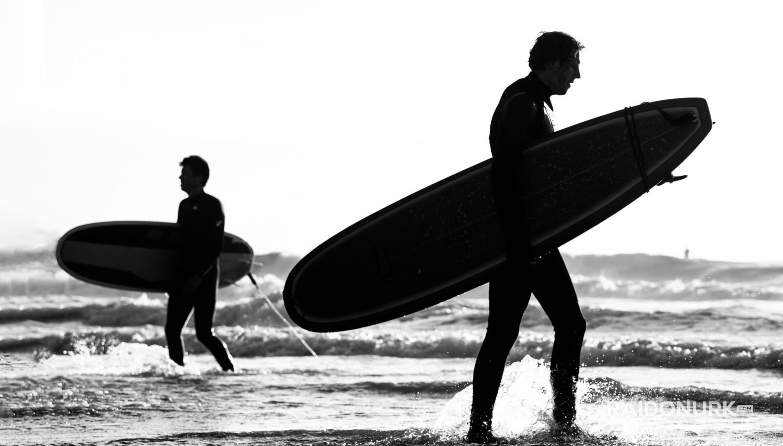 Black and white fine art photographs of surfers in action and at rest, silhouetted against bright skies and dramatic waves, capturing the essence of surfing in a minimalist, high-contrast visual style.